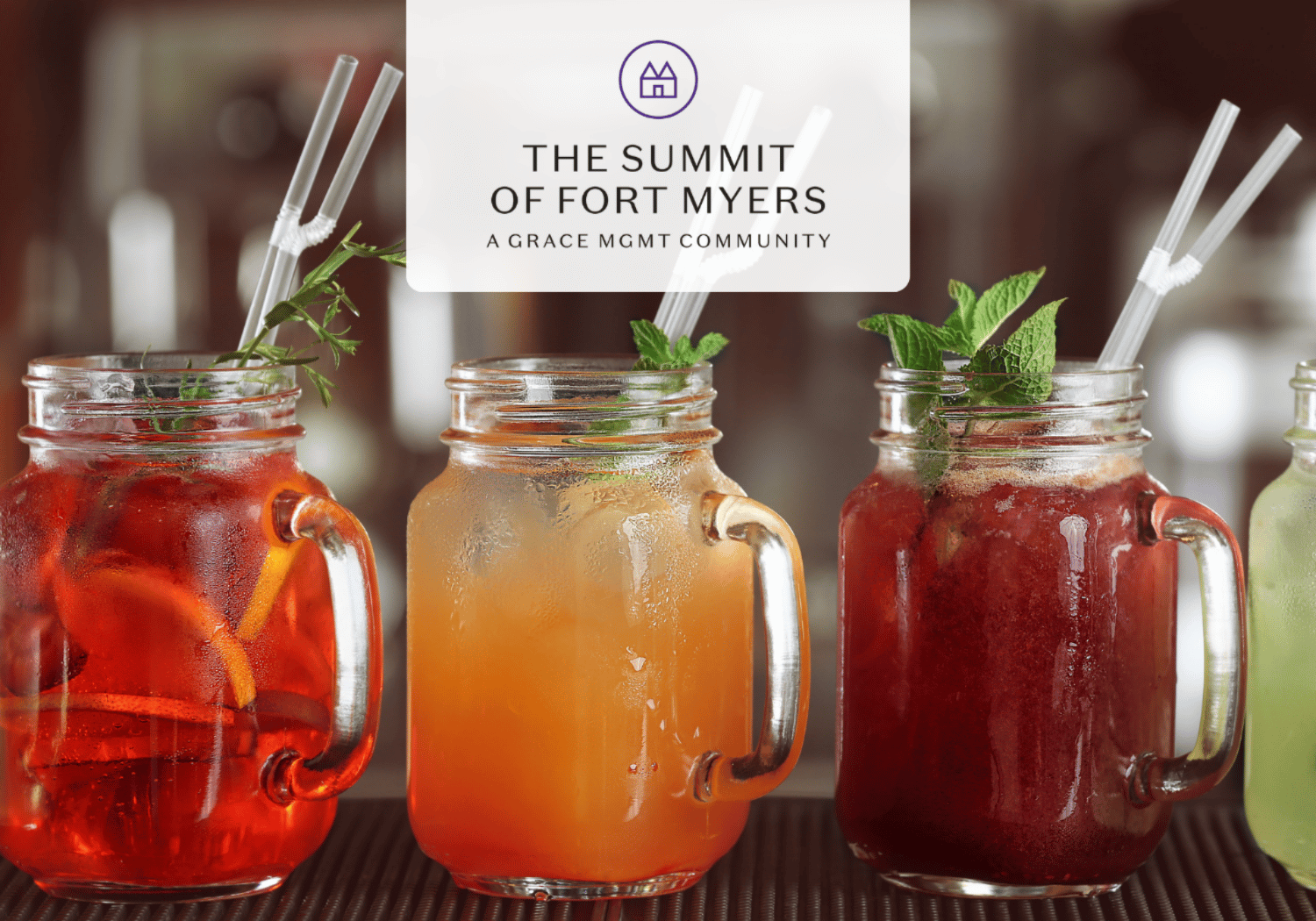 Three mason jars of iced colorful drinks with mint garnish sit on a bar, a banner with 'The Summit of Fort Myers' hangs above.