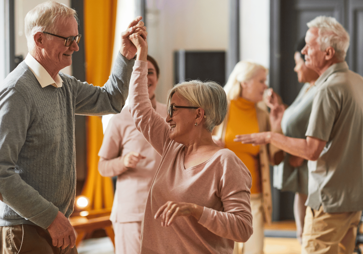 Older adults dancing together, a man and a woman high-fiving while smiling in a social gathering indoors.